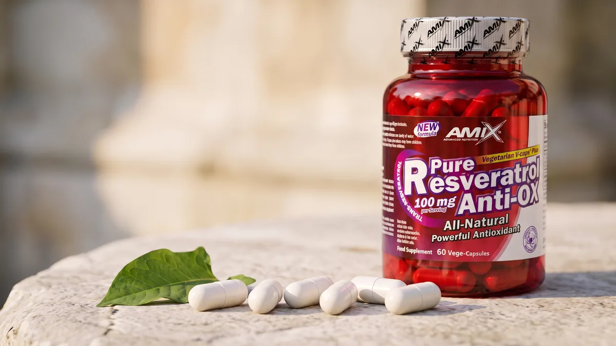 Sześć białych kapsułek roślinnych na kamieniu, w tle słoik Amix Pure Resveratrol